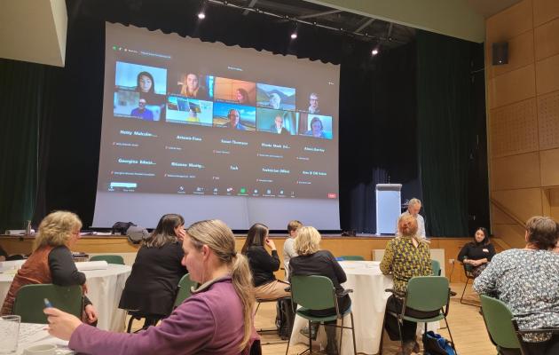 Image of attendees at the event and a big screen with Zoom hybrid event