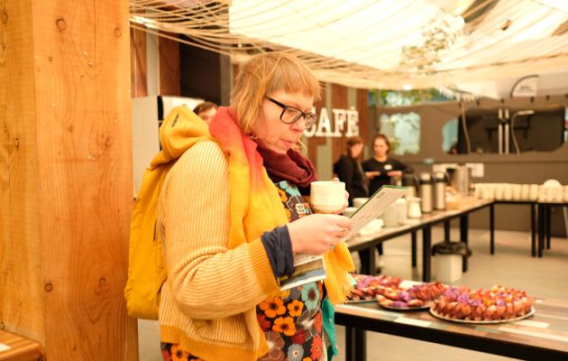 Attendee reads programme with coffee and tea behind them