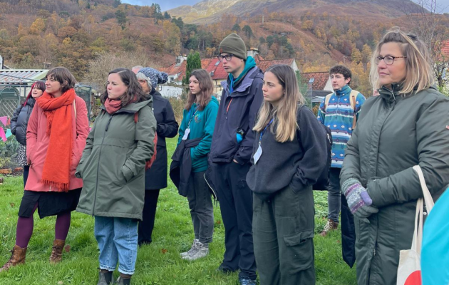 Image of attendees on a study visit, standing outside on grass listening to a presentation